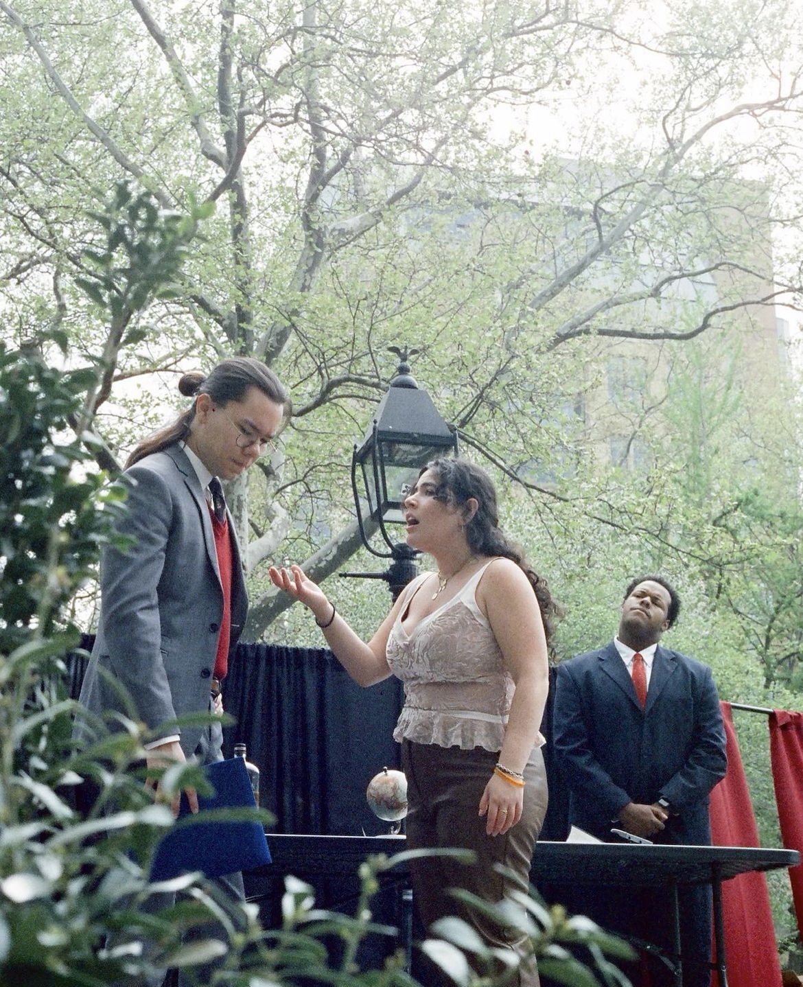 King Lear (2023) At an outdoor theater performance, a young woman argues with a disappointed man. Behind them, a young man watches with a thoughtful expression.