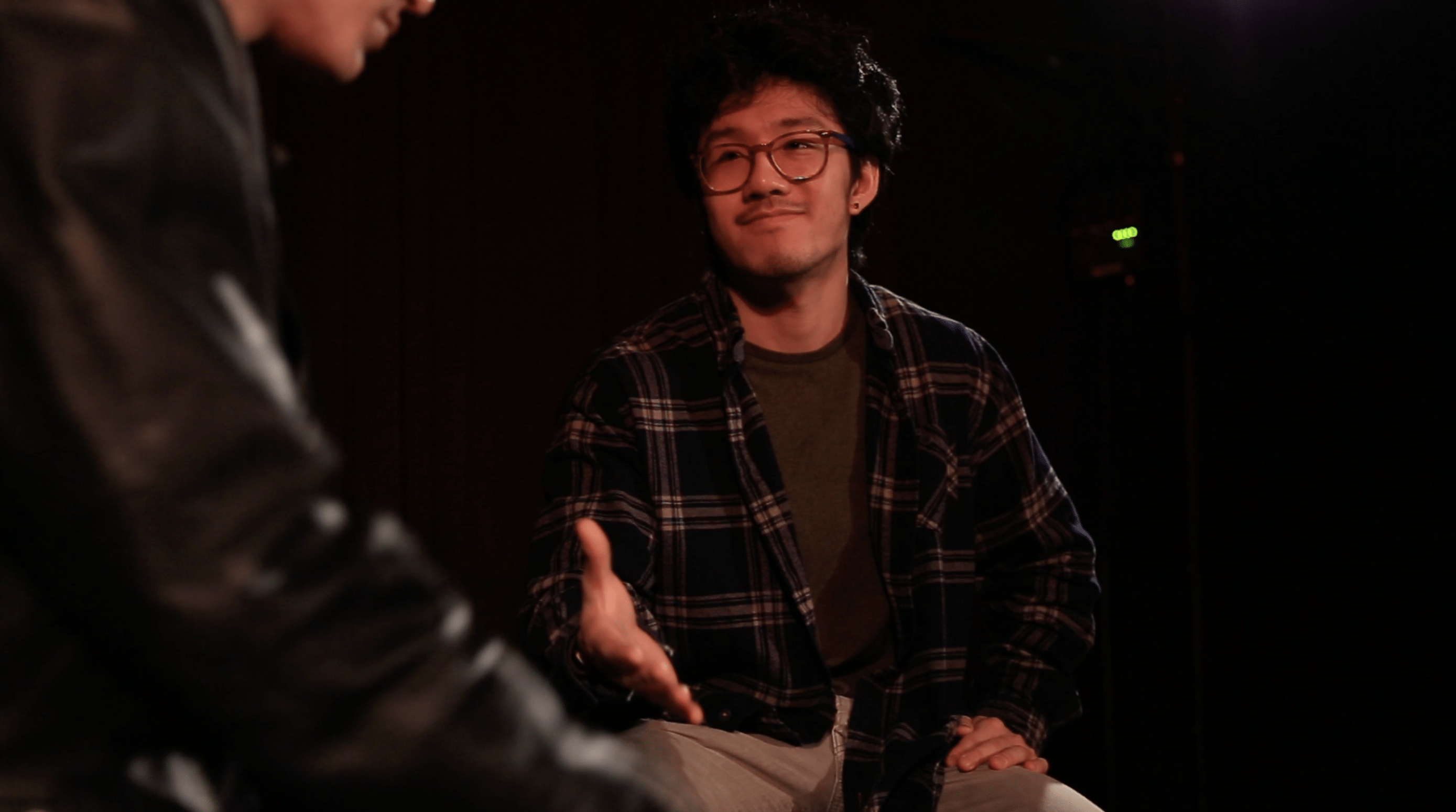 A young man extends a hand to another, expecting handshake. He smiles kindly.