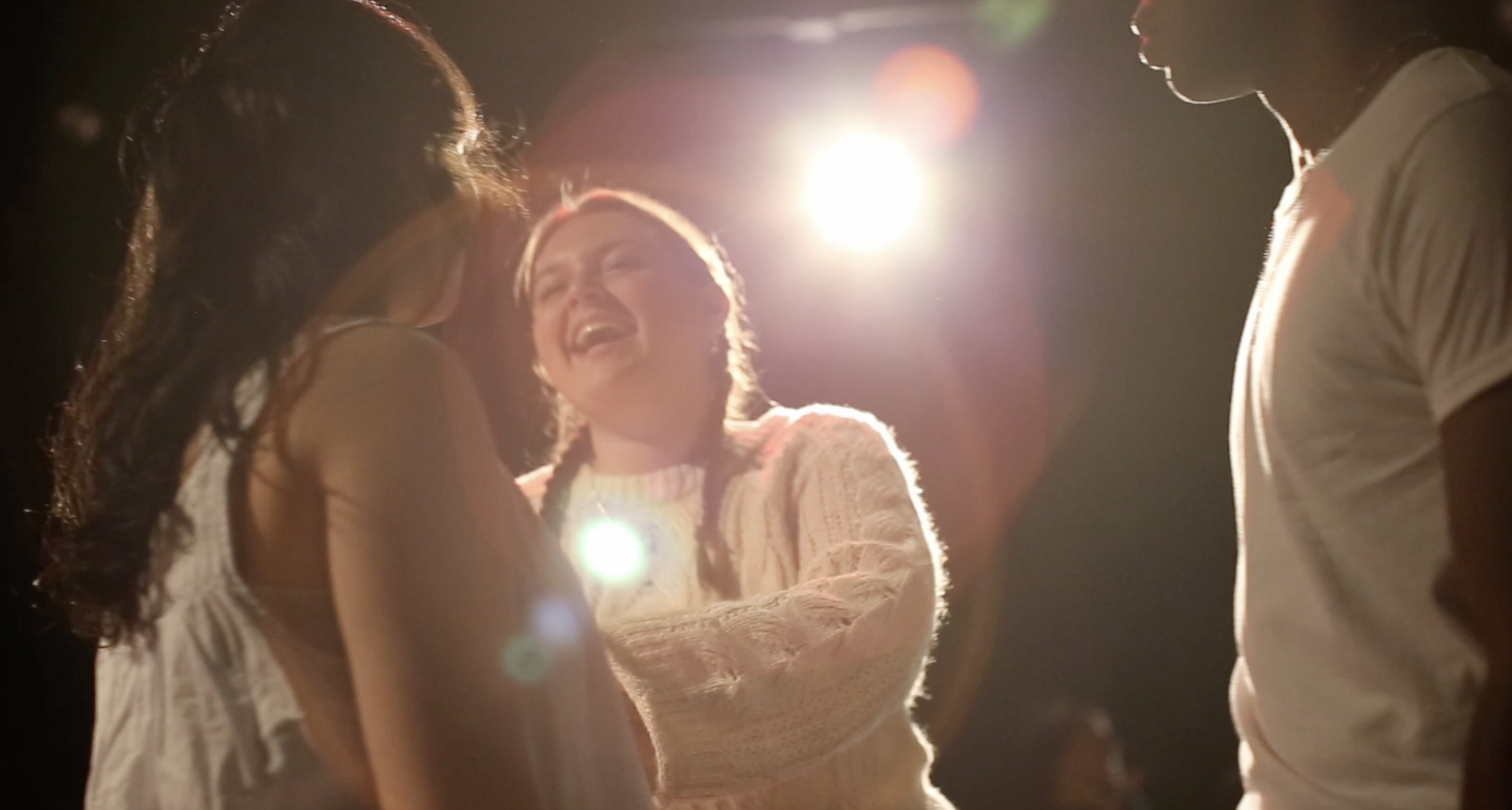 Bloody Passion BTS A girl in a sweater beams at two of her actors. A spotlight shines down on all of them.
