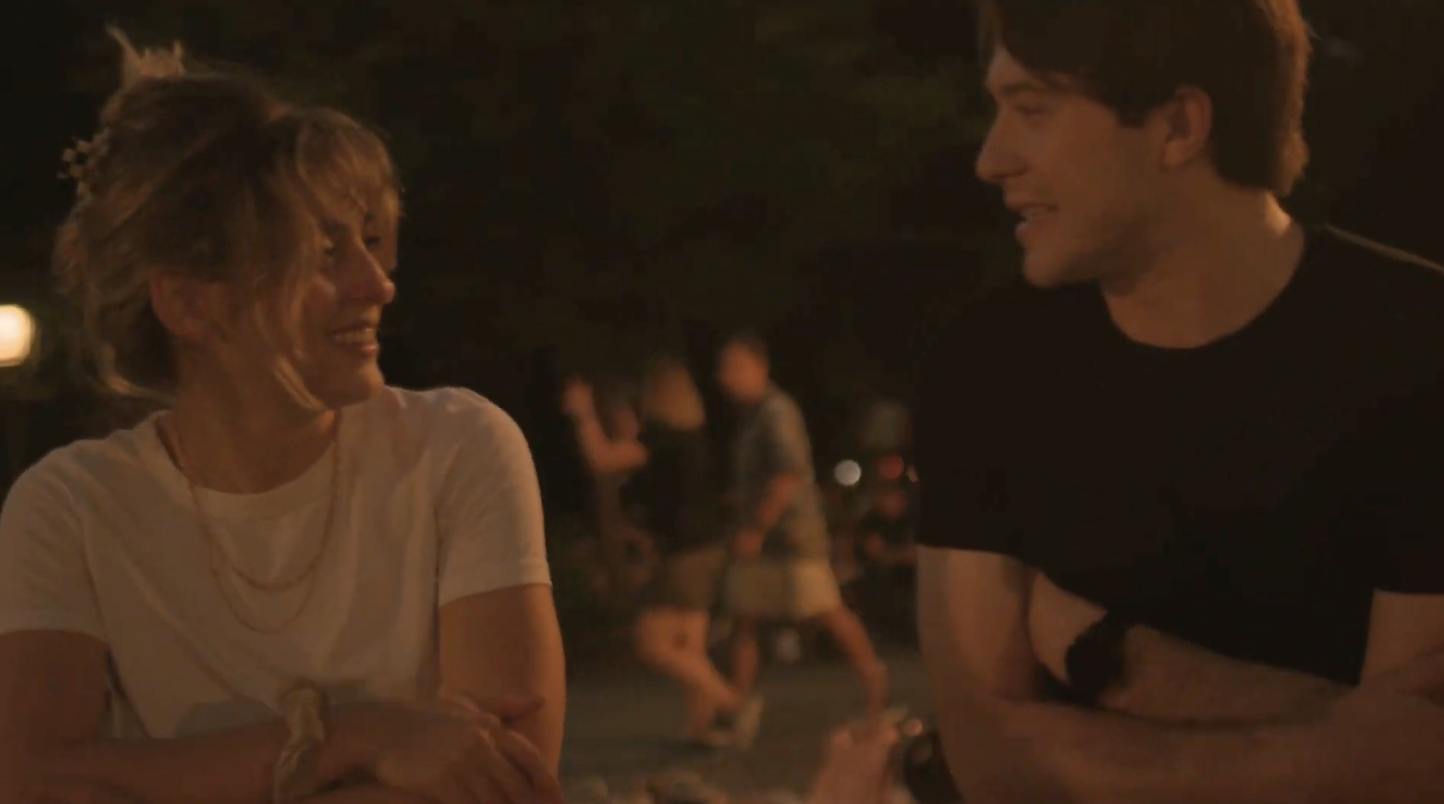 Two young people cross their arms awkwardly. They stare at each other. One wears black the other wears white.