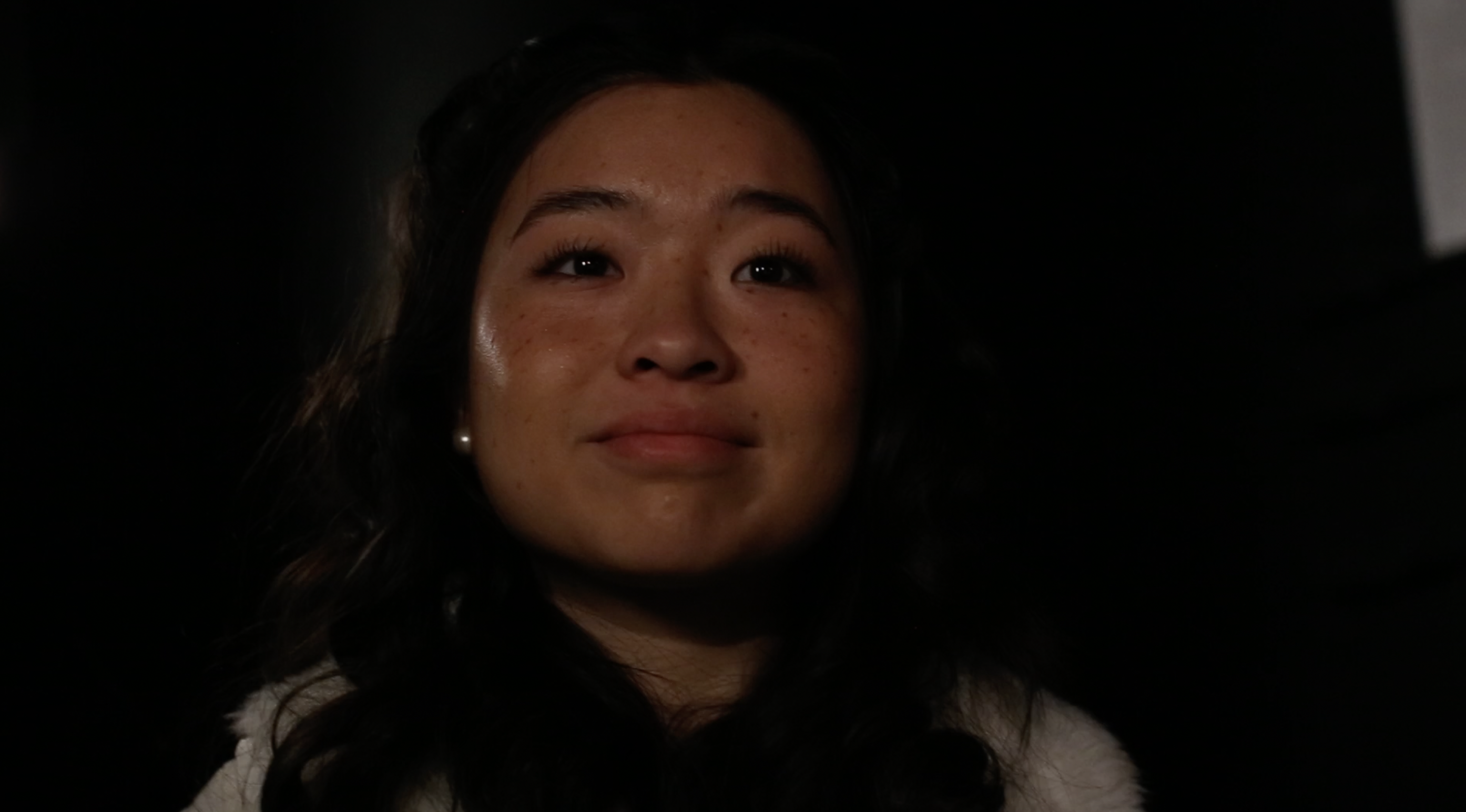 A young woman has a heartfelt expression. Only her face against a dark background is visible