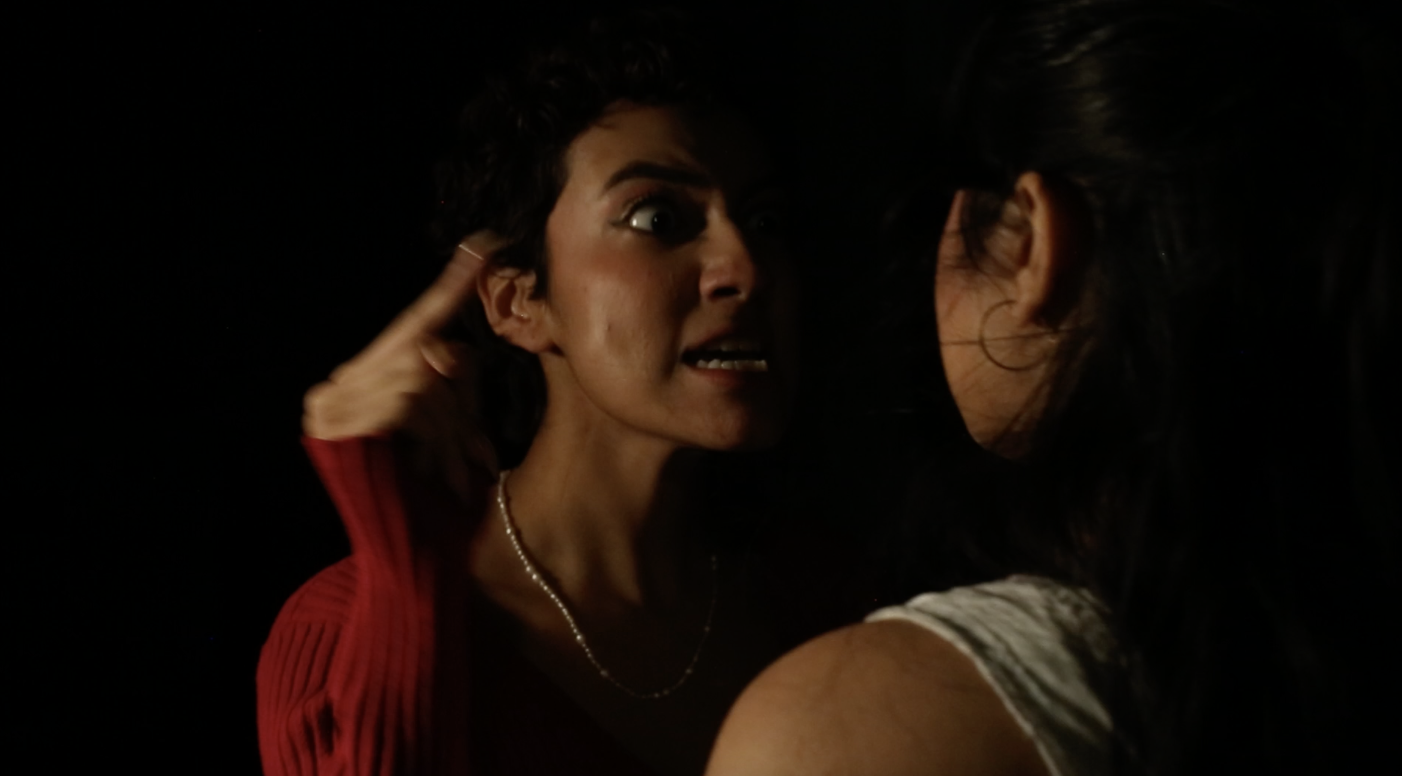 A young woman scolds another. They are backstage in the dark.