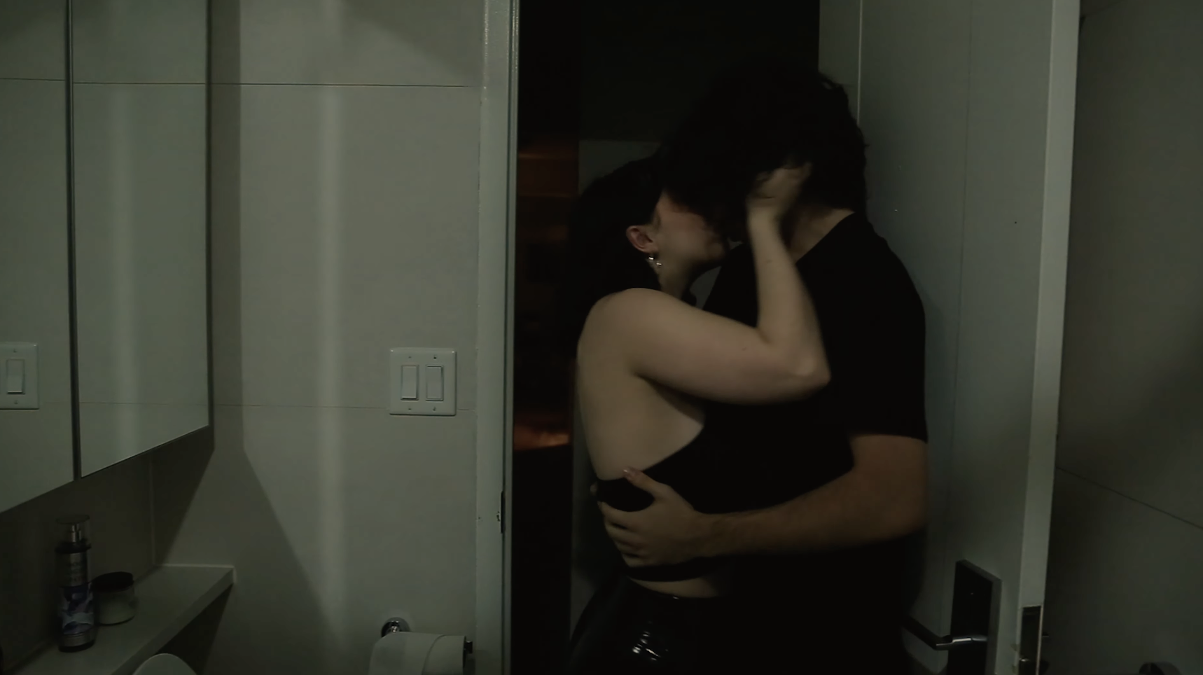 Two college students kiss in a bathroom.